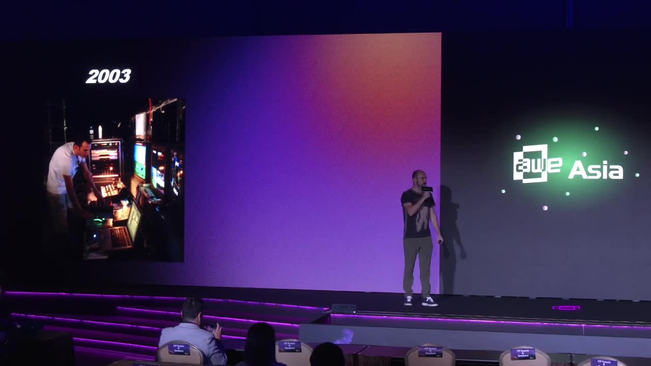 On the AWE Asia main stage, mid-talk, with a photo of a 2003 live-visuals mixing desk on the screen behind